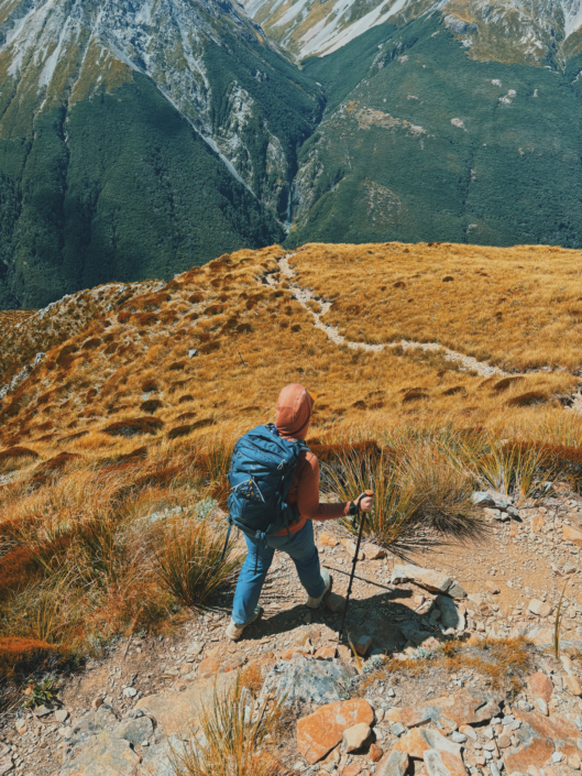 Hiking down Avalanche Peak in New Zealand using trekking poles on a steep rocky descent, demonstrating their value on alpine hikes