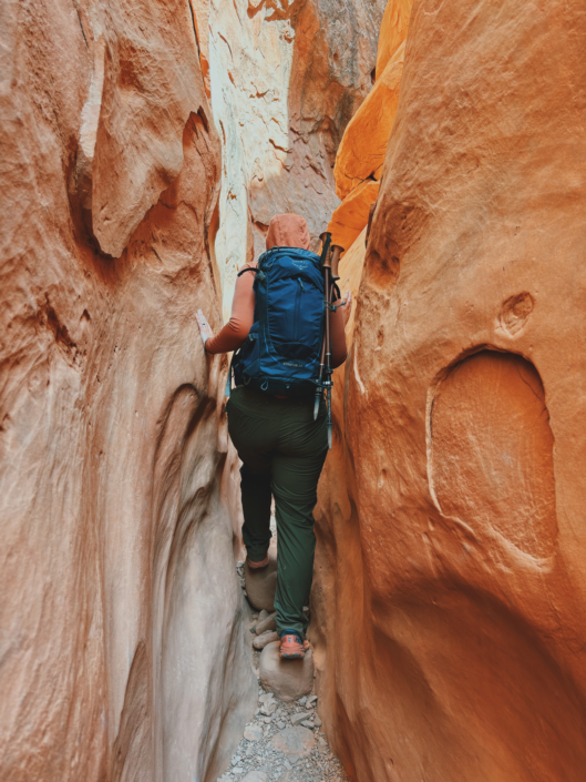 Trekking poles strapped to a backpack while hiking through a narrow slot canyon, showing when trekking poles are worth bringing but not using