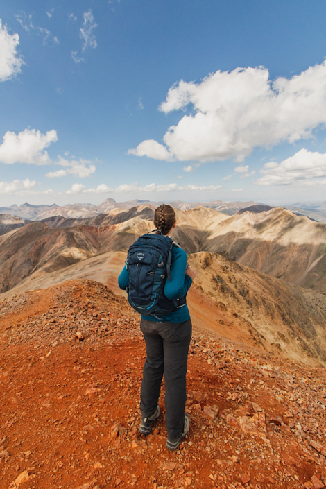 Emma overlooking rugged alpine ridge while hiking 14ers with expansive mountain views and blue sky on Redcloud Peak