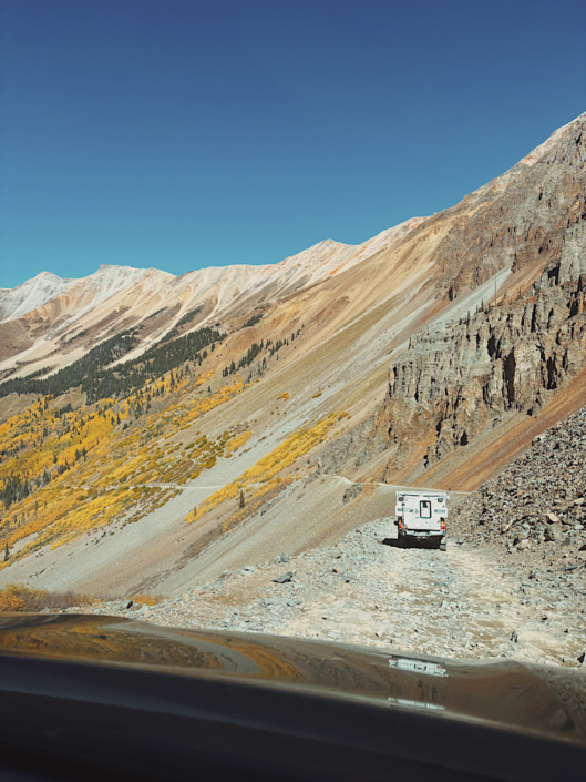 Driving Ophir Pass Colorado in a 4WD vehicle with a narrow mountain road and another truck camper ahead