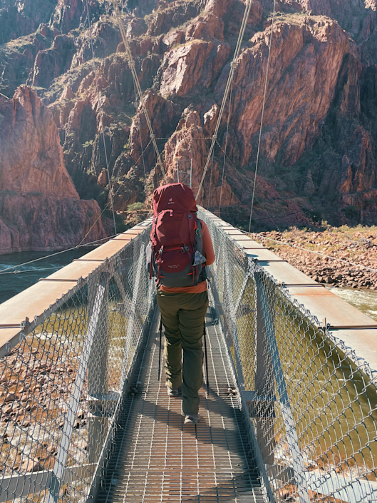 Emma wearing hiking boots while crossing the Colorado River suspension bridge at the bottom of the Grand Canyon during a backpacking trip