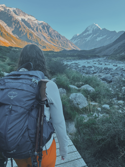 Hiking near Mount Cook in New Zealand with trekking poles strapped to a backpack, showing are trekking poles worth it for varied terrain