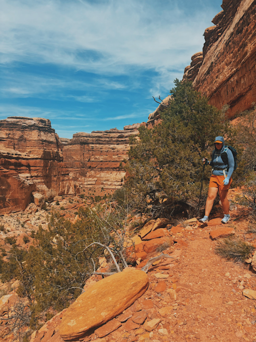 Hiking the Harvest Scene Loop in the Maze Utah with trekking poles near the edge of the canyon walls