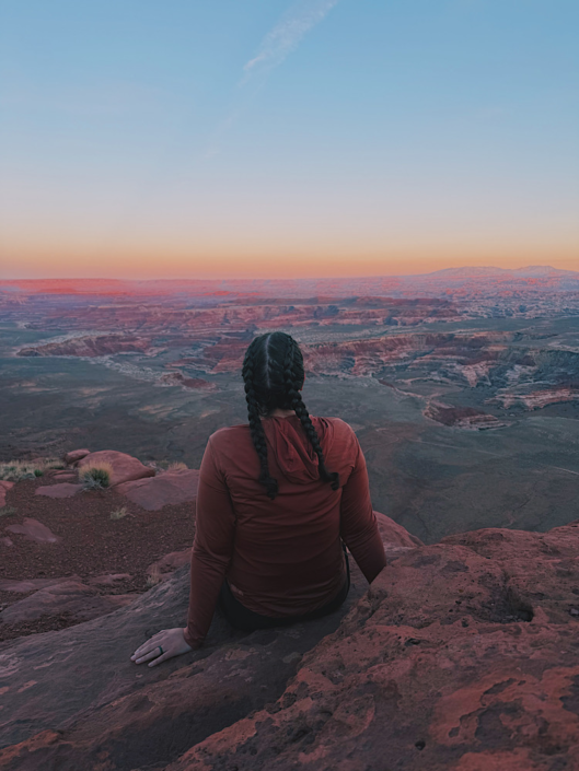 Emma sitting at Panorama Point at sunset overlooking the Maze in Canyonlands with expansive desert canyon views