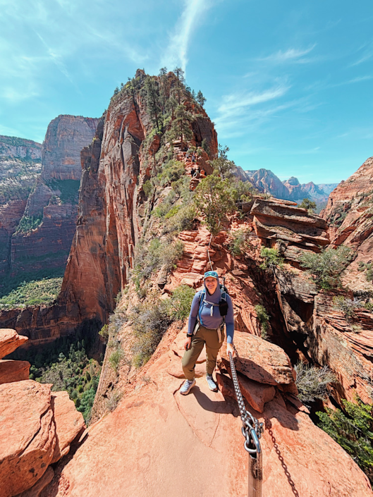 Hiker holding the chain section of the Angels Landing hike with Zion Canyon visible in the background