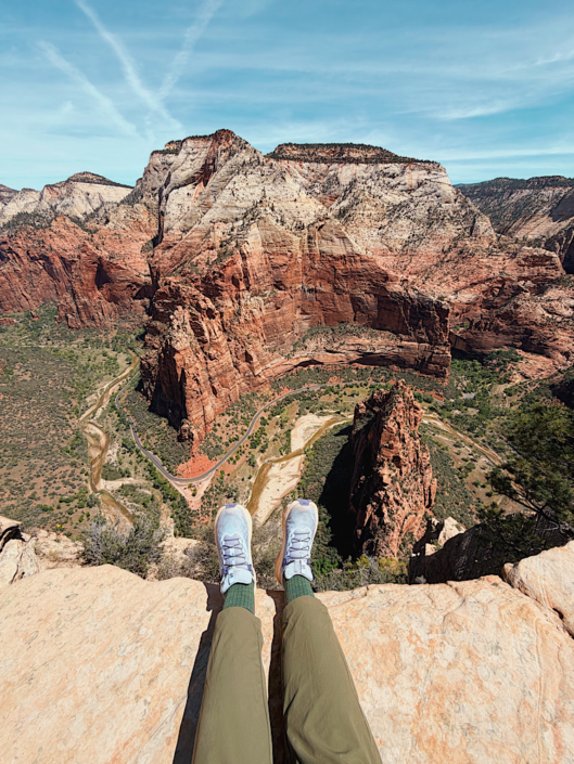 Feet positioned at the edge of the Angels Landing hike summit overlooking a dramatic drop into Zion Canyon