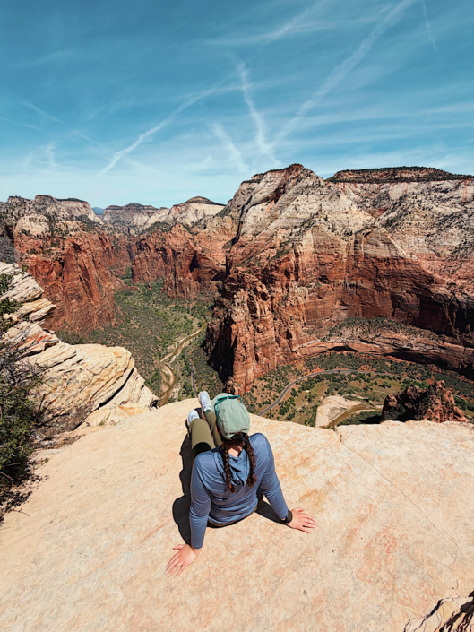 Emma sitting on cliff at the summit of the Angels Landing hike in Zion National Park overlooking Zion Canyon