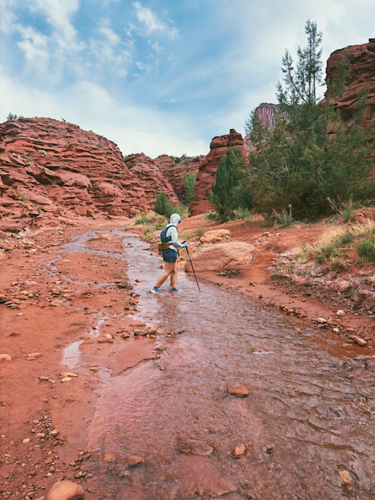 Crossing Professor Creek with trekking poles on the Mary Jane Slot Canyon hike near Moab before entering the narrow canyon