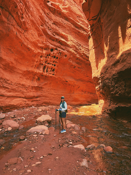 Hiker standing beneath towering canyon walls in Mary Jane Slot Canyon near Moab, Utah with glowing reflected light on the rock walls