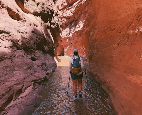 Hiking through the narrowest section of Mary Jane Slot Canyon in Utah with shallow water flowing through the slot canyon