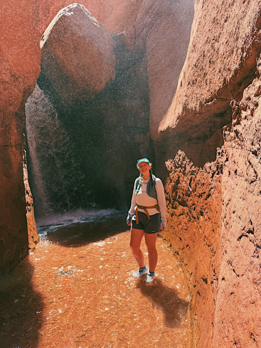 Standing in the water below the waterfall at the end of the Mary Jane Slot Canyon hike near Moab, Utah