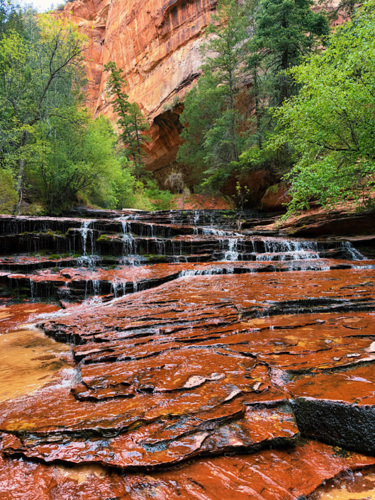 Cascading waterfall flowing over red rock terraces on The Subway hike in Zion National Park