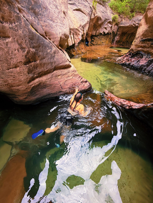 Hiker swimming through a cold pothole in the narrow Zion Subway slot canyon in Zion National Park