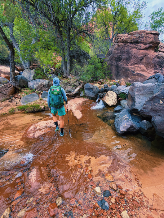 Hiker walking through a waterfall with large boulders along The Subway trail in Zion National Park