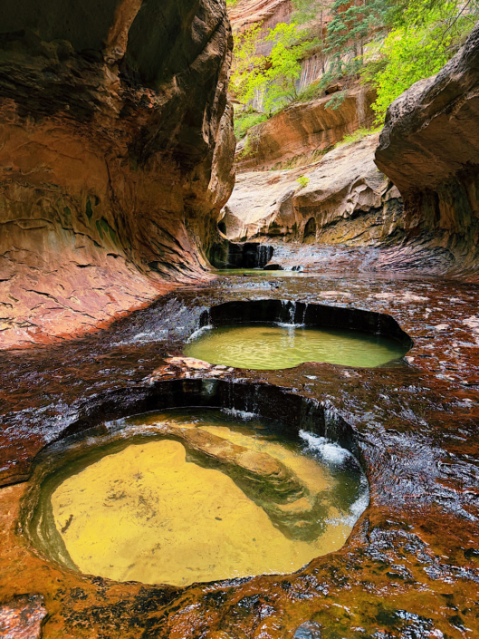Large sandstone potholes filled with clear water inside The Subway slot canyon in Zion National Park