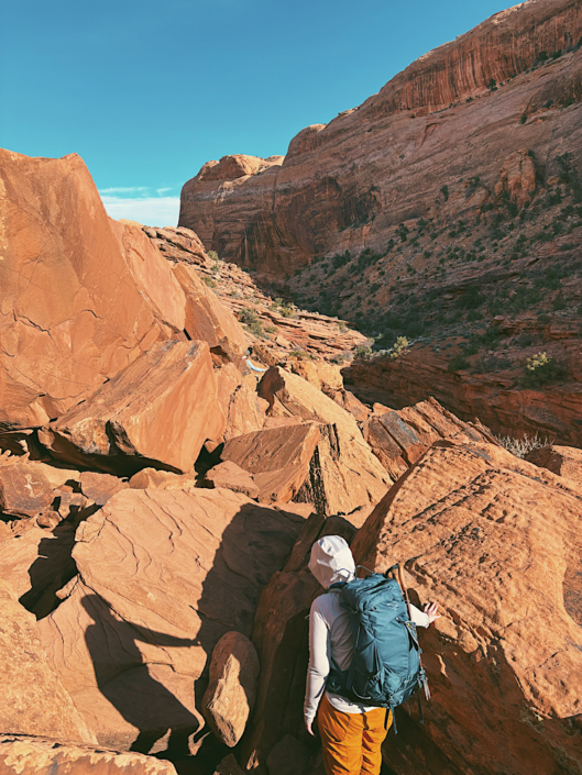 Hiker scrambling over large boulders on the Syncline Loop in Canyonlands National Park.