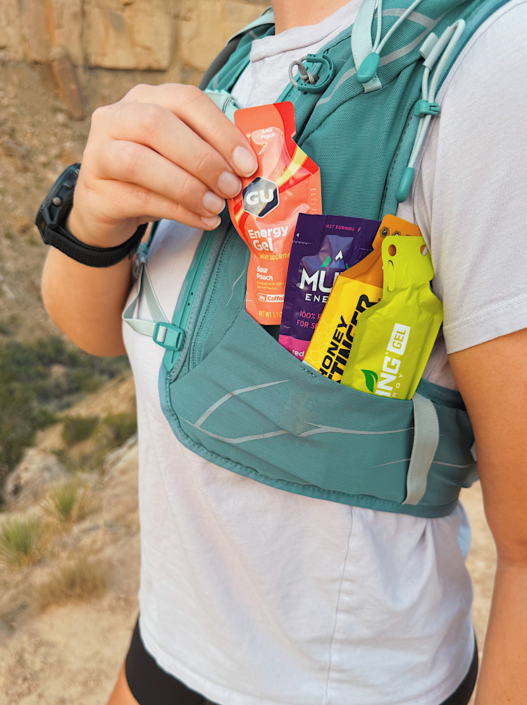 Hiker pulling a GU energy gel from a running vest with Muir Energy, Honey Stinger, and Spring Energy in the pocket