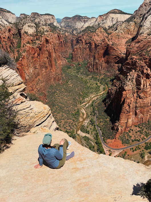 Sitting at the summit of Angels Landing overlooking Zion Canyon and the winding road far below in a Zion vs Bryce National Park comparison.
