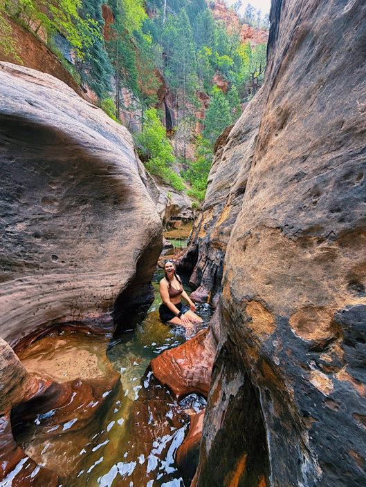 Sitting on a rock in the Subway slot canyon in Zion National Park, one of the park's most unique hikes in a Zion vs Bryce National Park comparison.