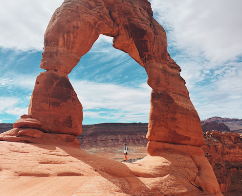 hiker standing under delicate arch on an arches national park hiking trail