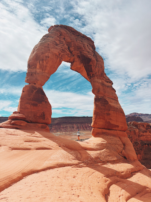 hiker standing under delicate arch on an arches national park hiking trail