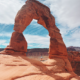 hiker standing under delicate arch on an arches national park hiking trail