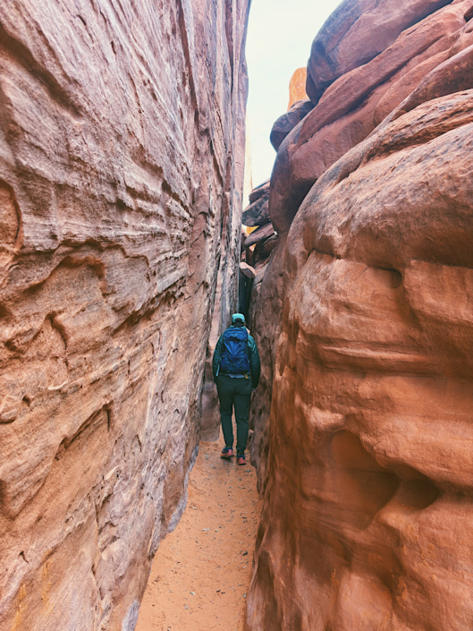 Hiker walking through a narrow sandstone canyon in the desert