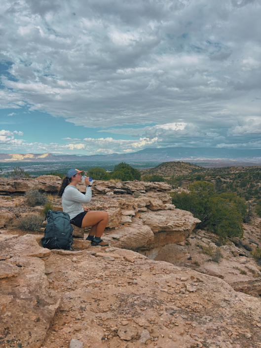 Hiker drinking electrolytes from a water bottle while resting on a desert trail