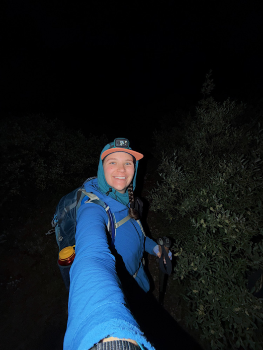 Hiker wearing a headlamp and backpack while hiking with trekking poles at night