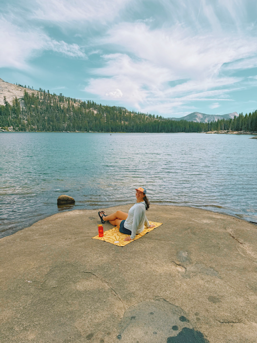 Hiker sitting on a Nomadix towel beside an alpine lake