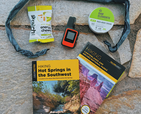 Hiking guidebooks, Garmin inReach, sunscreen, energy chews, and cooling neck tie arranged on a rock