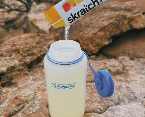 Pouring Skratch Labs electrolyte powder into a water bottle while hiking