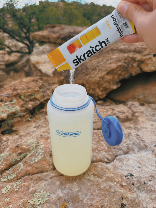 Pouring Skratch Labs electrolyte powder into a water bottle while hiking