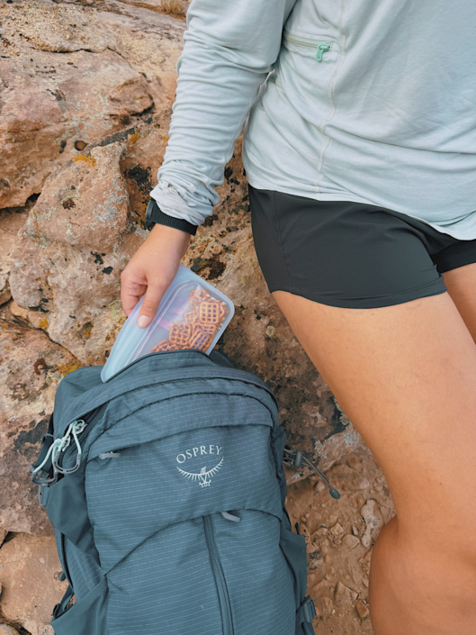 Hiker packing pretzels in a reusable Stasher bag into a hiking backpack