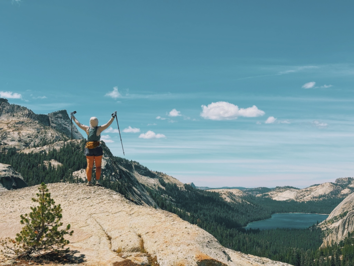 Hiker holding trekking poles at an overlook above Tenaya Lake in Yosemite