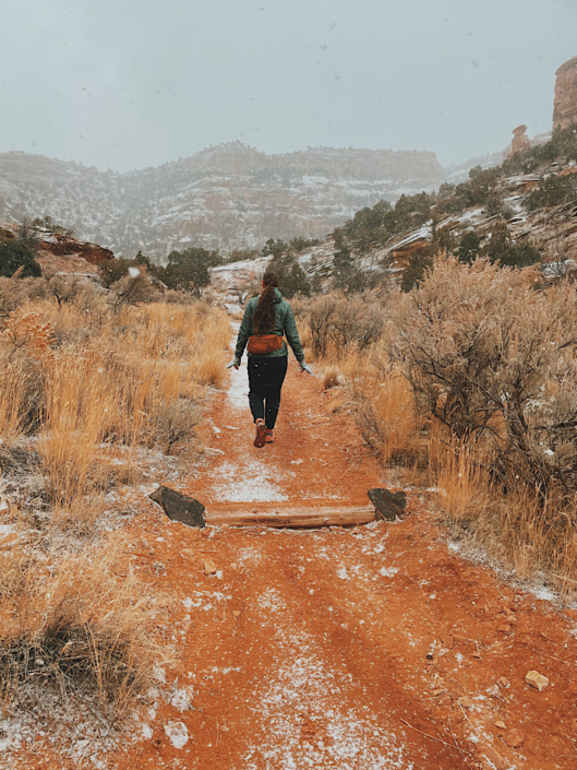Hiker walking a red dirt desert trail during a winter snowstorm