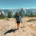 Hiker standing on Sentinel Dome with trekking poles and Half Dome rising above the mountains in the background.